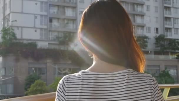 Primo piano di giovane donna asiatica in piedi sul balcone, guardando da parte poi voltandosi, guardando la fotocamera e sorridendo - Filmati, video