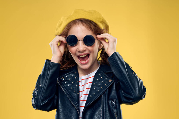 Wesoła dziewczynka w okularach przeciwsłonecznych i kapelusz styl życia studio żółty tło moda - Zdjęcie, obraz