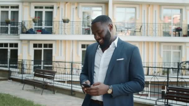 Usmívající se afro-muž posílá zprávy ven. Obchodní muž relaxace s telefonem - Záběry, video