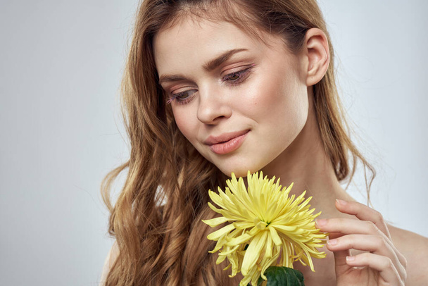 Portret van een mooie vrouw met een gele bloem op een lichte achtergrond charmante glimlach model rood haar - Foto, afbeelding