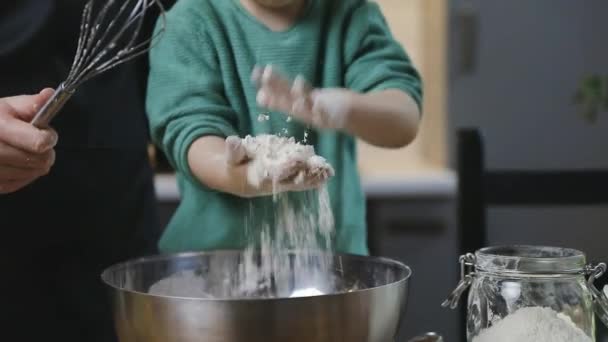 Poika lapsi ja äiti valmistelevat taikinaa lämpimässä kodikkaassa keittiössä puupöydällä. Perhe-elämän ja harrastusten käsite. - Materiaali, video