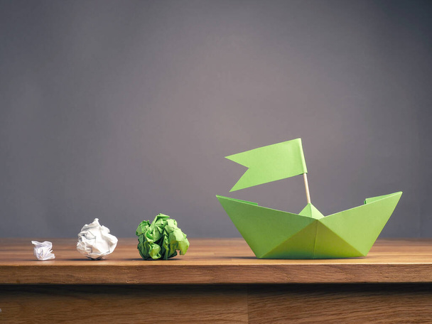 Teamwork business concept with crumpled paper and a paper boat on a wooden office table with space for text, ecology or green ideas concept - 写真・画像