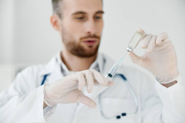 γιατρός με ιατρική ρόμπα κρατά μια σύριγγα στο χέρι του και μια ένεση εμβολίου. - Φωτογραφία, εικόνα