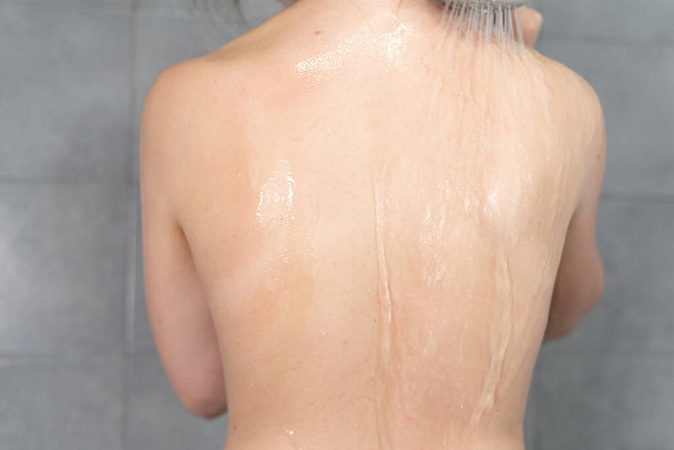 Recortada la espalda de una joven hermosa mujer, se lava en la ducha en casa. Una corriente de agua tibia fluye sobre un hermoso cuerpo femenino. Copiar espacio - Foto, imagen