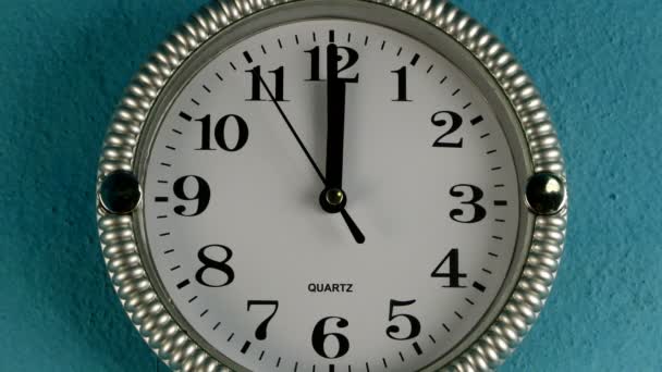 Křemenné nástěnné hodiny s druhou rukou běží ve směru hodinových ručiček. Hodiny ukazují dvanáct hodin. Na staré modré zdi. Detailní záběr. - Záběry, video