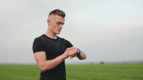 The athlete is standing on the field and choosing the type of training on his watch. The camera is rotating around him. Running training. 4K - Footage, Video
