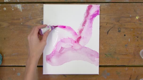 Górny widok artystki maluje abstrakcyjny różowy obraz, wylewa różową farbę z tuby na wilgotne płótno - Materiał filmowy, wideo