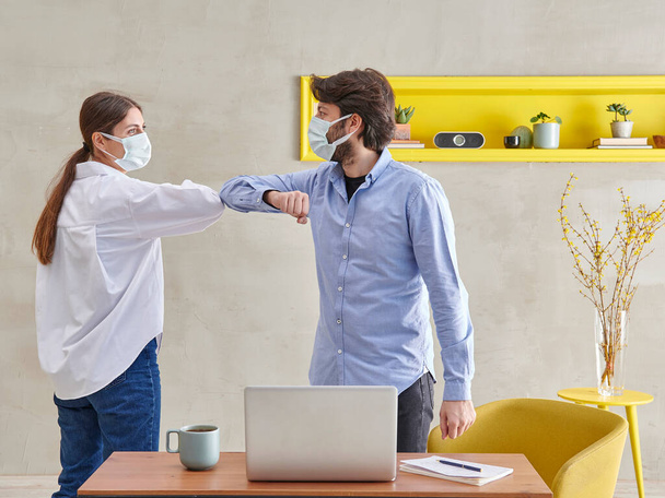 Deux personnes portant un masque facial sur le lieu de travail accueillent le concept de distance sociale pendant la pandémie. - Photo, image