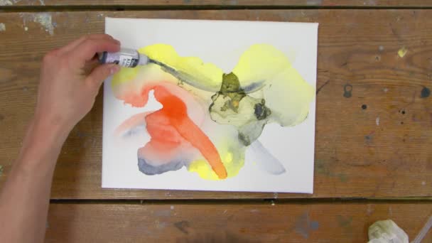 Arte fluido. Pintura colorida abstracta. Vista superior de artista masculino vierte pintura negra sobre lienzo húmedo y utiliza pincel para distribuirlo - Imágenes, Vídeo