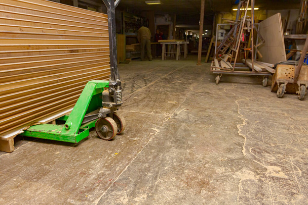 Hand pallet truck laden with arranged thin glued profiles of planks on it in the carpenter's workshop warehouse. - Photo, Image