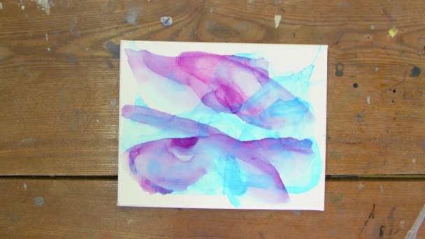 Vista dall'alto dell'artista dipinge un quadro astratto, usa pennello per dipingere forme astratte con vernice viola su tela bagnata - Filmati, video