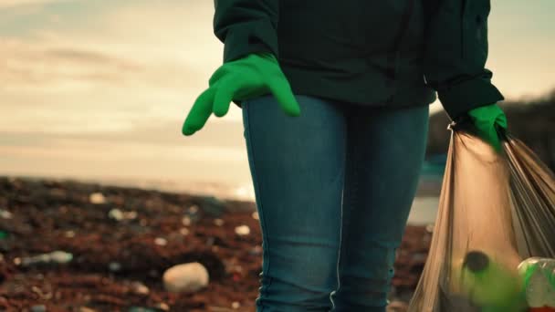 Добровольча жінка в гумових рукавичках бере пляшку з землі і кладе її в мішок для сміття. Повільний рух. М'який фокус. Концепція охорони навколишнього середовища
. - Кадри, відео
