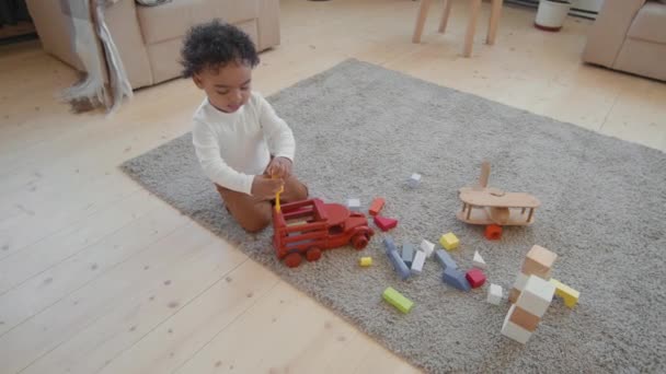 Handheld-Hochwinkel-Ortung des entzückenden Kleinkindes, das im Wohnzimmer auf einem Teppich sitzt und mit seinem Spielzeug spielt - Filmmaterial, Video