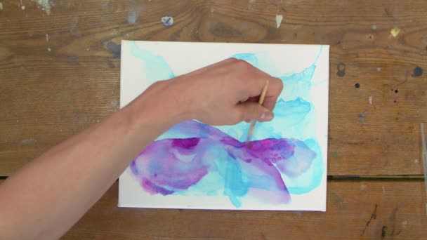 Top view a művész fest egy absztrakt képet, ő használ ecsetet festeni absztrakt formák lila festék nedves vászonra - Felvétel, videó
