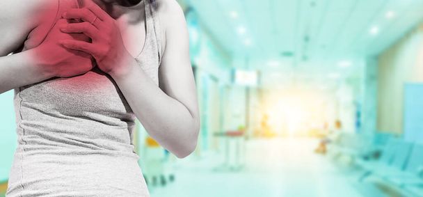 Young woman holds the chest in the heart.Symptoms of red spot heart pain on blue blur background of the hospital.Communicates the symptoms of heart disease,which is a serious disease.May cause death. - Photo, Image