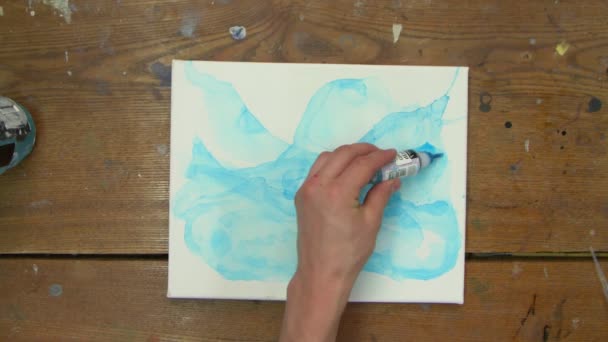 Vista superior do artista pinta um quadro abstrato, ela pinta formas abstratas com tinta azul na tela molhada e usa pincel para distribuí-lo - Filmagem, Vídeo