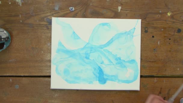 流体芸術。抽象的なカラフルな絵画。女性アーティストのトップビューは、青い抽象的な画像とキャンバスにピペットから水を注ぎ、それを配布するために絵筆を使用しています。 - 映像、動画