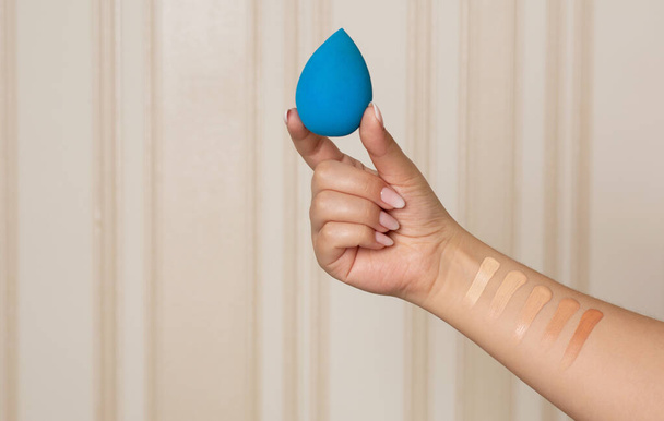 Maquillaje artista sosteniendo blender belleza azul y tener muestras de fundación líquida en su mano. Espacio para texto - Foto, Imagen