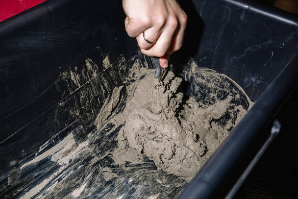 Uma pessoa mistura cimento e água em um recipiente para obter a mistura acabada. O processo de construção, uma das etapas da decoração. A fazer gesso. Close-up. - Foto, Imagem