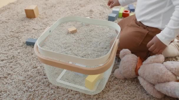 Close up slowmo of unrecognizable toddler kneeling on rug and putting his building blocks into basket - Footage, Video