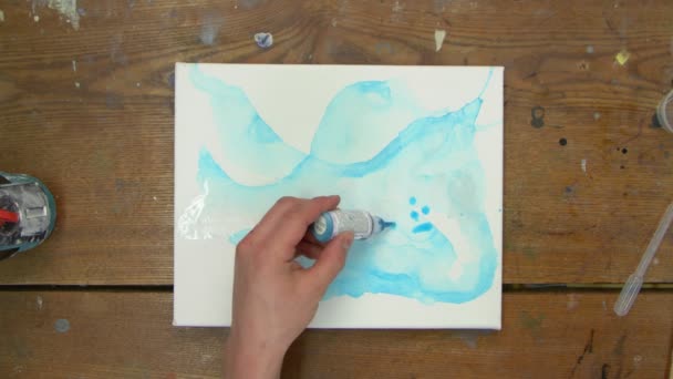 Top näkymä naisartisti maalaa abstrakti kuva, hän käyttää sinistä maalia märkä canves ja jakaa sen siveltimellä - Materiaali, video