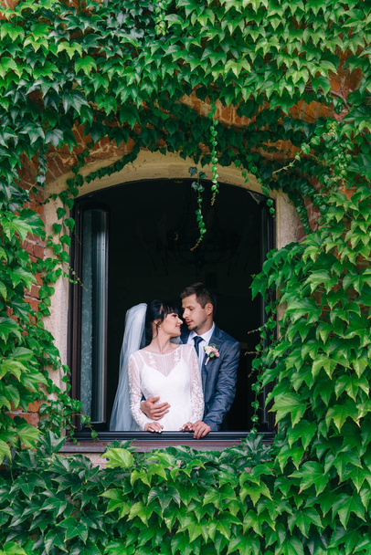 krásná a mladá nevěsta a ženich stojí u okna v paláci.. - Fotografie, Obrázek
