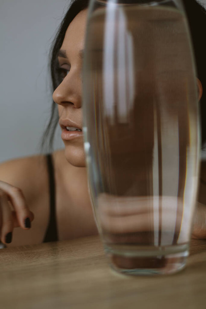 A beautiful brunette girl hid her face in profile behind a vase of water, leaving only her nose - Fotoğraf, Görsel