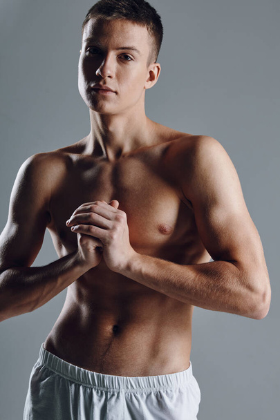 sexy Athletinnen mit aufgeblasenem Oberkörper, die Hände vor der Brust auf grauem Hintergrund haltend  - Foto, Bild