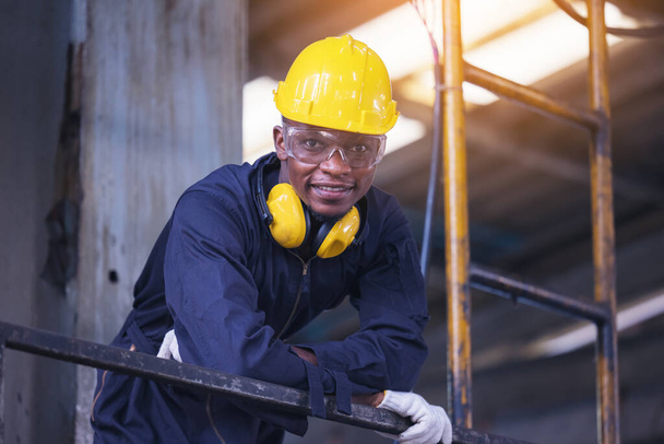 Retrato trabajador hombre con casco amarillo y protección del oído en fábrica, tono oscuro - Foto, Imagen