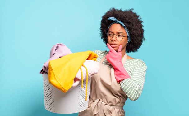 black afro woman smiling with a happy, confident expression with hand on chin, wondering and looking to the side. housekeeping concept.. household concept - Photo, Image