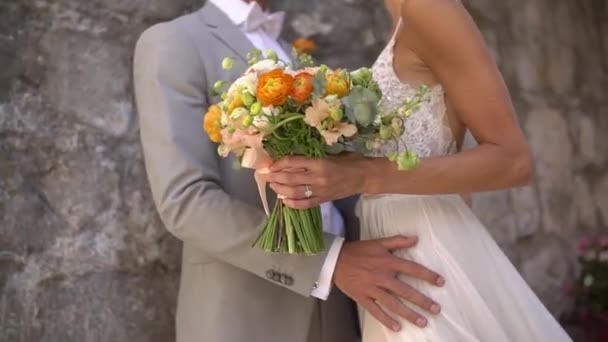 The bride and groom are embracing at the stone wall of an old house, close-up - Video