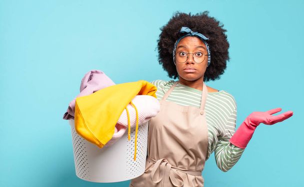 black afro woman feeling puzzled and confused, doubting, weighting or choosing different options with funny expression. housekeeping concept.. household concept - 写真・画像