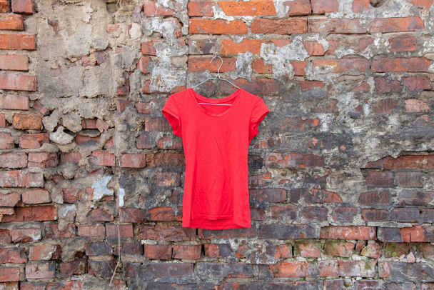 camiseta roja colgando de una percha en una pared de ladrillo en la calle, ropa de mujer de moda - Foto, imagen