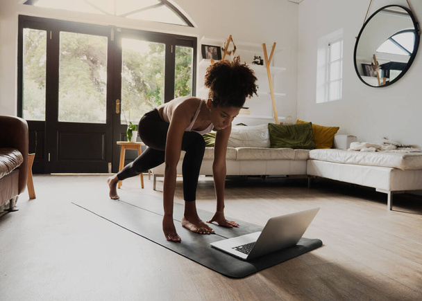 Afroamerikanischer Teenager praktiziert Yoga-Flow und schaut Video auf Laptop in moderner Lounge  - Foto, Bild