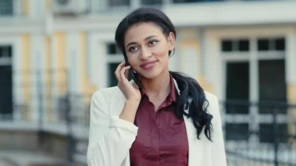 Una mujer de negocios sonriente hablando por teléfono afuera. Mujer de raza mixta llamando al aire libre - Metraje, vídeo