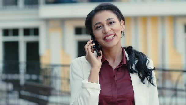 Una empresaria sonriente hablando por teléfono afuera. Señora de la raza mixta hablando al aire libre - Metraje, vídeo