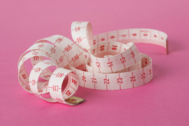 white and red dressmaker's ribbon wrapped around itself and isolated on pink background - Photo, Image