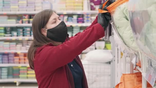Chica con máscara y guantes contra el virus elige manta caliente en una tienda - Metraje, vídeo