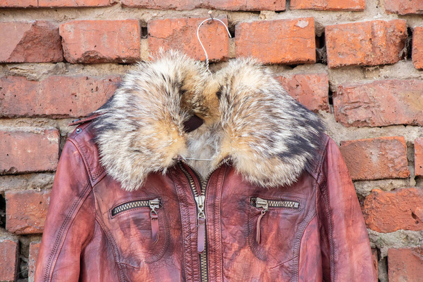 veste hiver femme en cuir à fourrure rouge suspendue à un cintre sur un vieux mur de briques à l'extérieur pendant la journée, vêtements pour femmes - Photo, image