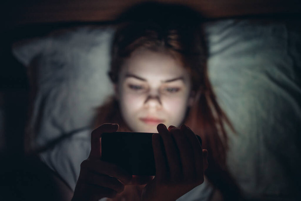 mujer con un teléfono en sus manos en la noche antes de acostarse emociones adicción comunicación - Foto, imagen