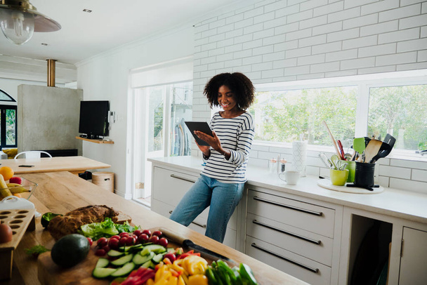 Mooie gemengde ras vrouw browsen tablet voor recept in de keuken thuis - Foto, afbeelding