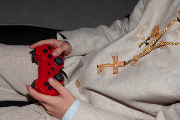 Detalle de un niño de comunión jugando videojuegos. Donde las manos de los niños se ven sosteniendo un controlador rojo. - Foto, imagen