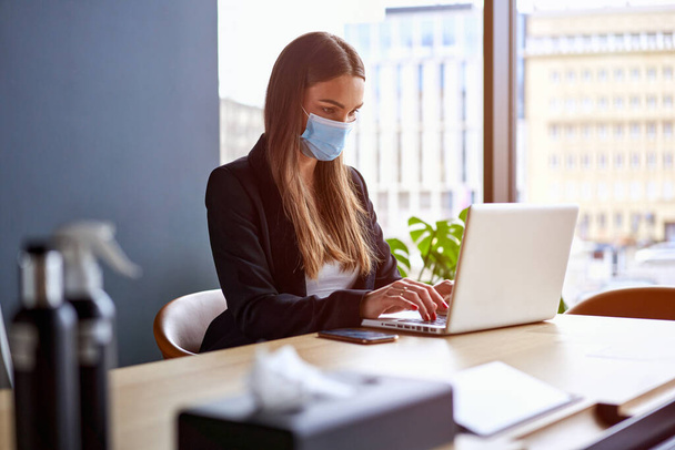 Businesswoman working on laptop wearing face masks protect from coronavirus in office - Valokuva, kuva