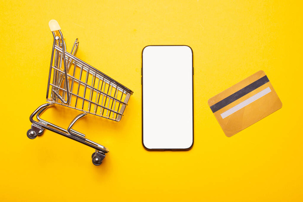 Malá nákupní vozík kreditní karta a smartphone s prázdnou obrazovkou pro copyspace - Fotografie, Obrázek