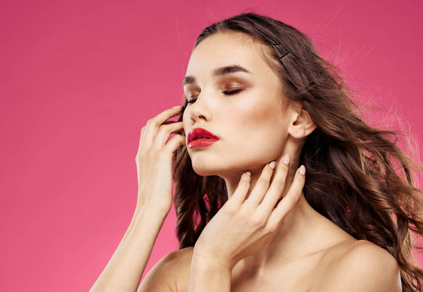 Sexy Brünette mit roten Lippen auf rosa Hintergrund berühren ihre Haare mit ihren Händen - Foto, Bild