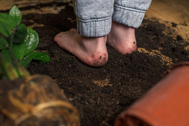 Niño descalzo de pie en el suelo disperso de una maceta - Foto, imagen