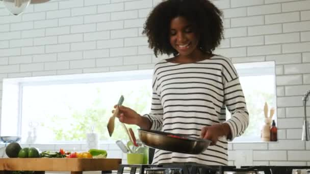 Krásná mladá smíšená rasa žena s úsměvem a vaření na pánvi smažení, obracející zelenina v pánvi - Záběry, video