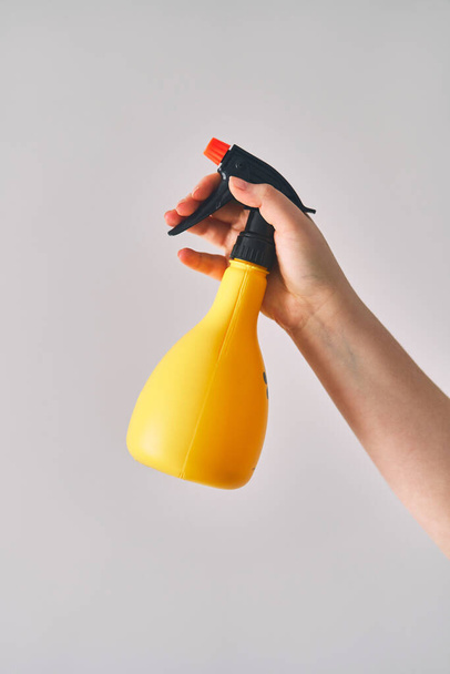 Une jeune femme tient un vaporisateur dans sa main. Flacon de pulvérisation jaune sur fond blanc. Photo de haute qualité - Photo, image