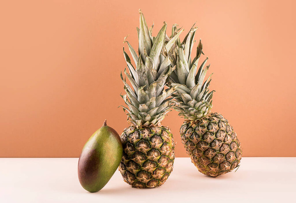 Dos piñas maduras con mangos, equilibrando la fruta sobre un fondo de color. Concepto de levitación alimentaria - Foto, Imagen