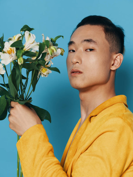 Vista lateral de um cara romântico em um casaco desabotoado, aparência asiática e um buquê de flores em sua mão - Foto, Imagem